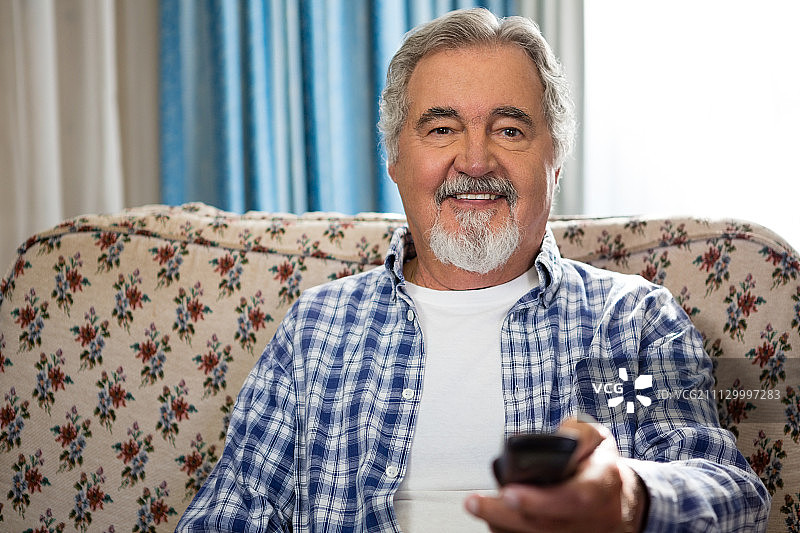 老人坐在沙发上操作遥控器的微笑肖像图片素材