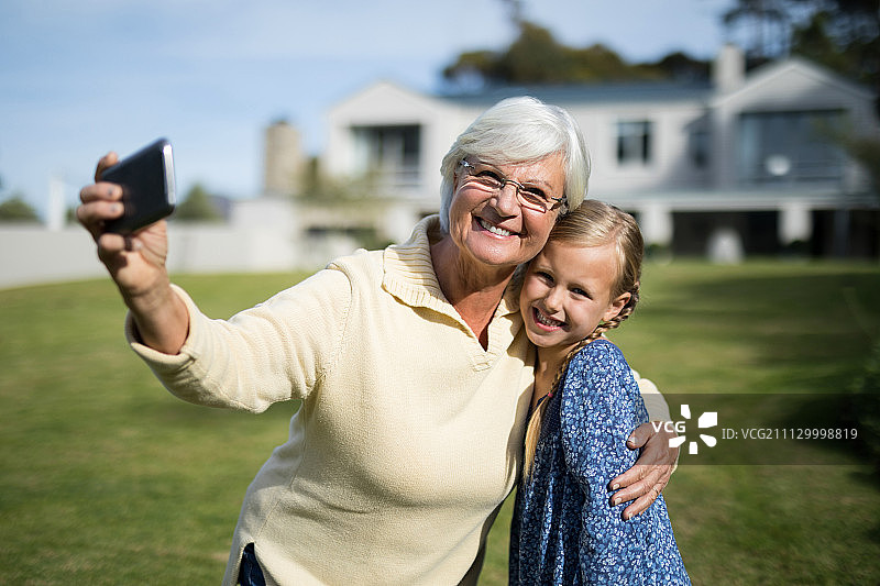 阳光明媚的一天，奶奶和孙女在花园里用手机自拍图片素材