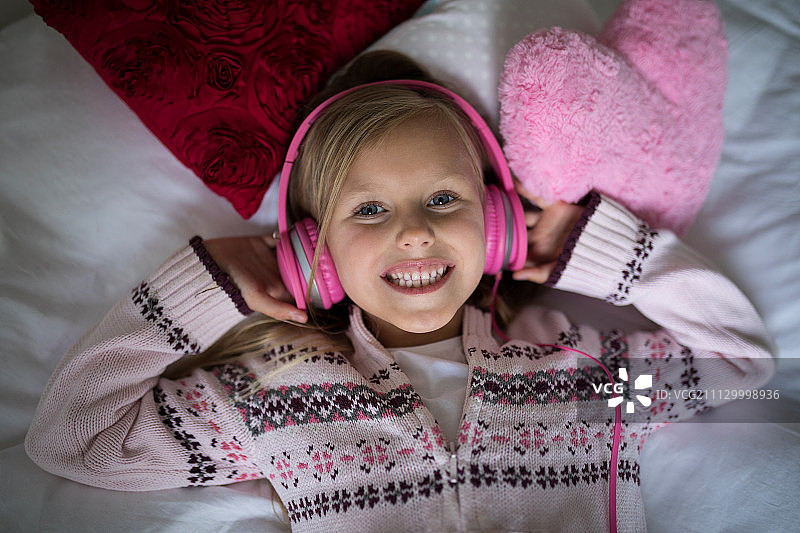 微笑的女孩躺在床上听耳机音乐图片素材