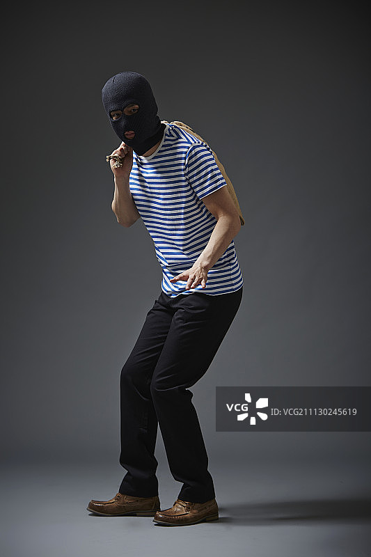 摄影棚拍摄的男人与黑色面罩和休闲服装穿着小偷拿着袋子图片素材