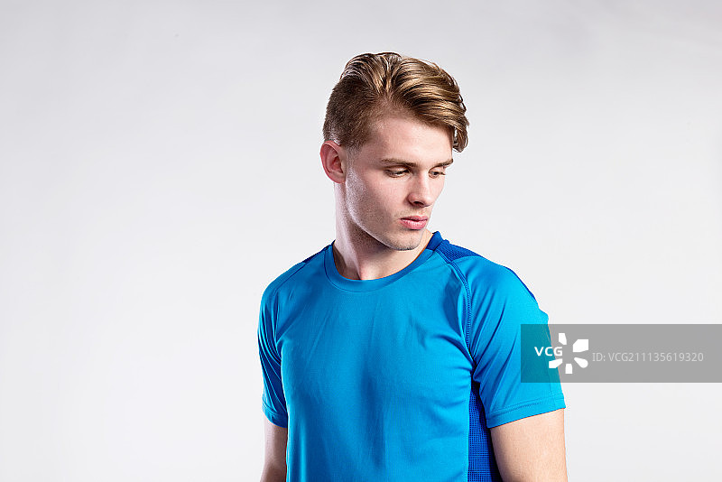 年轻帅气的潮男穿着蓝色运动t恤，在摄影棚拍摄。图片素材