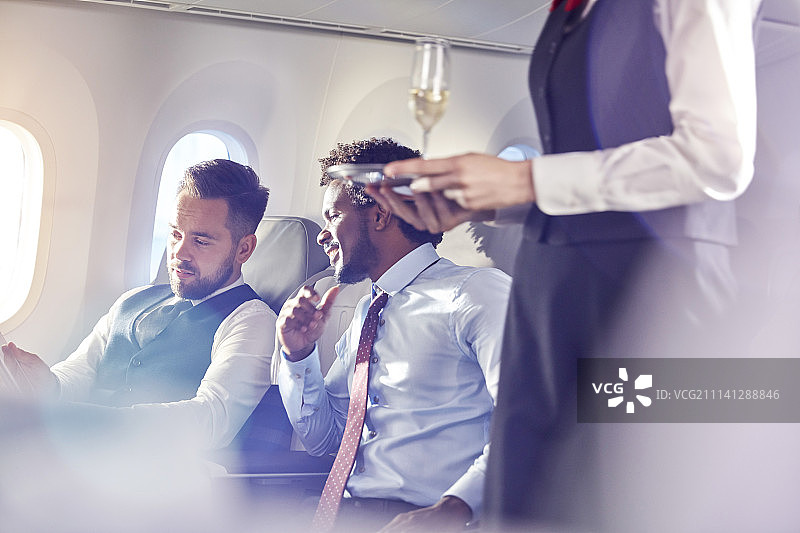 在飞机头等舱为商务人士提供香槟的空姐图片素材