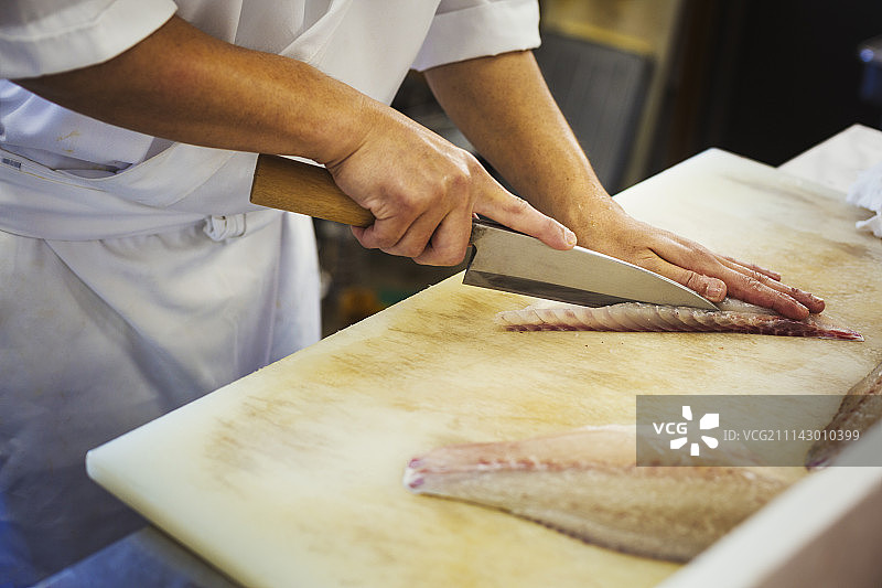 高角度的近距离厨师工作在一个日本寿司餐厅的柜台，切片鱼片。图片素材