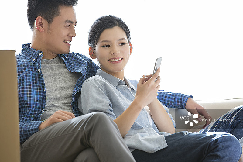 年轻情侣坐在沙发上看手机图片素材