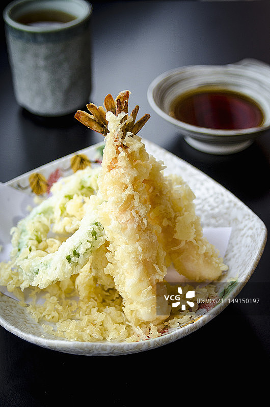 日式日式天妇罗配蔬菜和虾，用清淡的天妇罗面糊炸过，放在盘子里，黑色的桌子上，配以日式鱼汤蘸酱和绿茶图片素材