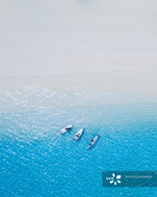 高角度的三个人放松在桨板在蓝色的水图片素材