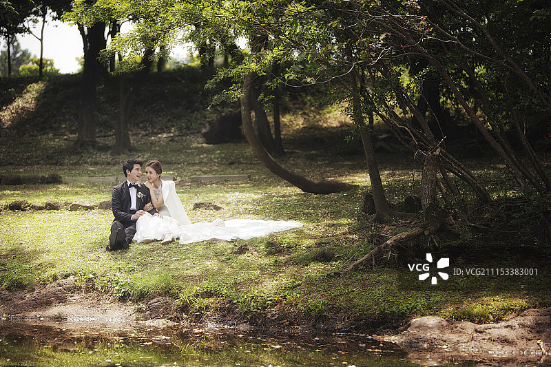 新娘和新郎互相倚靠坐在草地上图片素材