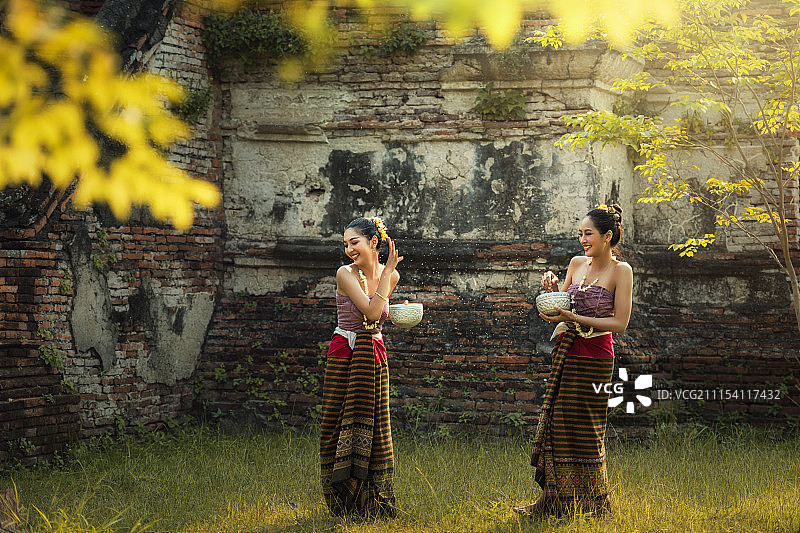 在泼水节，亚洲妇女穿着传统的泰国服装玩水花图片素材