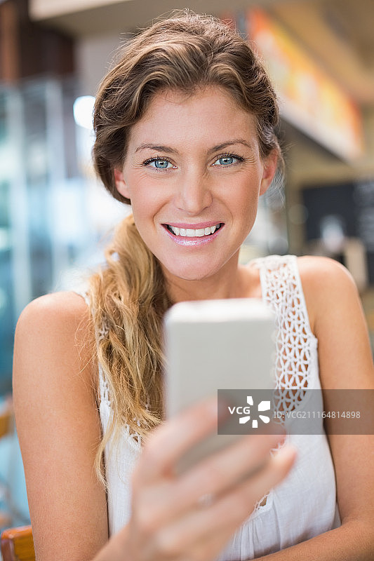 美丽的女人拿着手机，对着镜头微笑图片素材