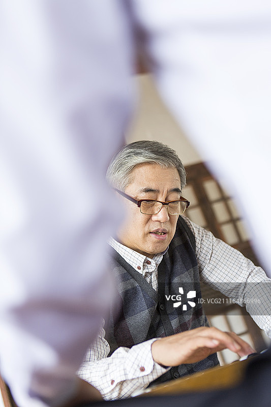 穿着西装的男人和坐在传统韩式房子地板上玩围棋的老人的照片图片素材