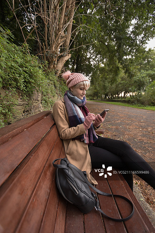 年轻女子坐在长椅上用手机图片素材
