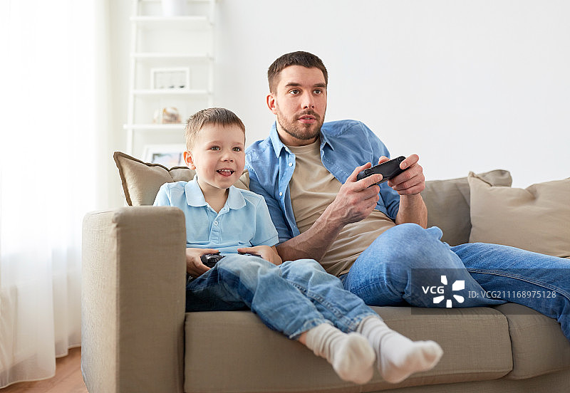 家庭，父亲和人们的概念-快乐的父亲和儿子与游戏手柄在家里玩电子游戏。父亲和儿子在家里玩电子游戏图片素材