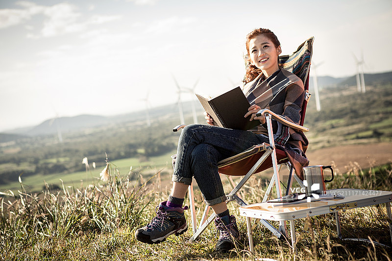 盖着毯子的女人坐在山顶上看书的照片图片素材