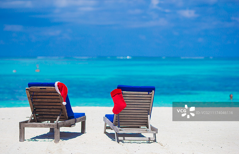 红色的圣诞帽和红色的圣诞袜在热带度假海滩躺椅上图片素材