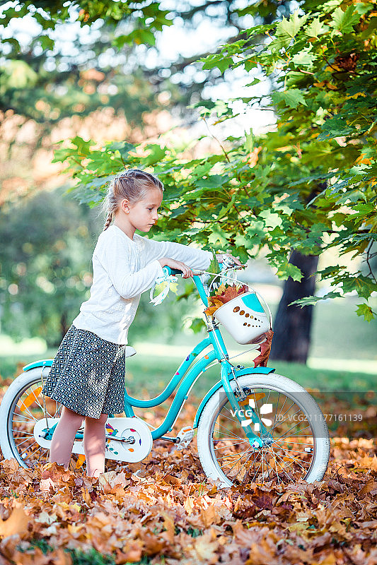 可爱的女孩在美丽的秋天骑自行车图片素材