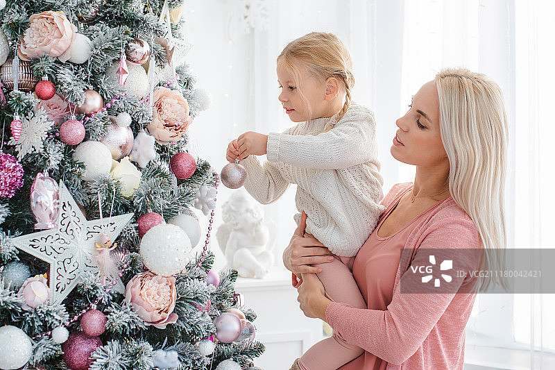 妈妈和女儿在室内装饰粉红色的圣诞树。图片素材