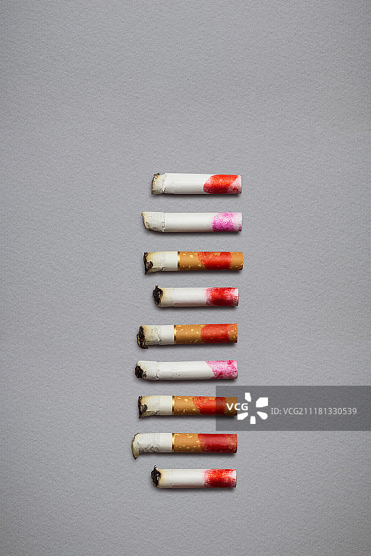 不同烟头的创意静物画，在灰色背景上涂上口红。图片素材