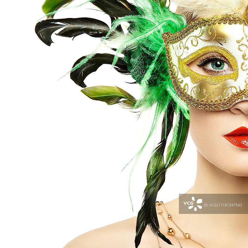 美丽的年轻女子在神秘的金色威尼斯面具。时尚照片。化妆面具与绿色羽毛图片素材