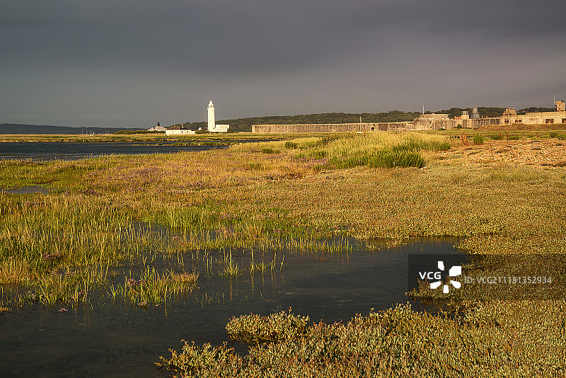湿地景观在暴风雨的天空日落朝向灯塔图片素材