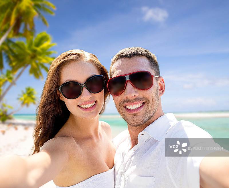 旅游、旅游和暑期度假概念——一对戴着太阳镜的微笑情侣在法属波利尼西亚的热带海滩上自拍。一对戴着墨镜的情侣在海滩上自拍。一对戴着墨镜的情侣在海滩上自拍图片素材