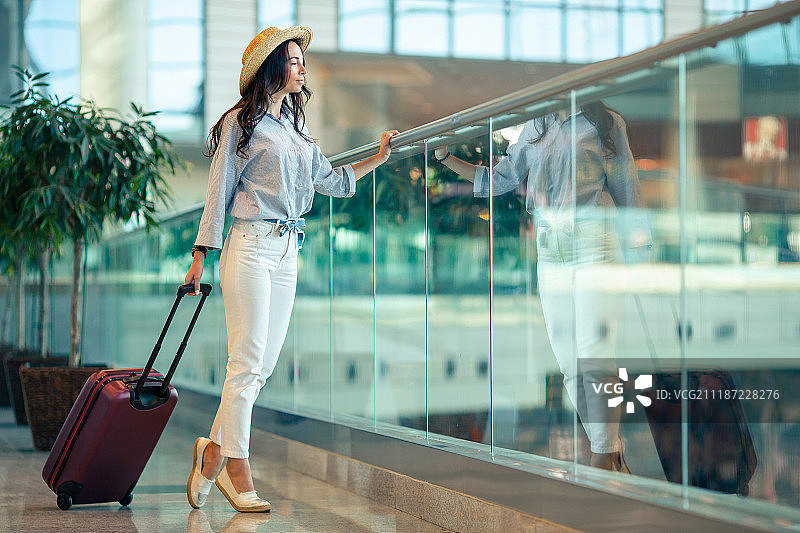 在国际机场戴着帽子拿着行李的年轻女子图片素材