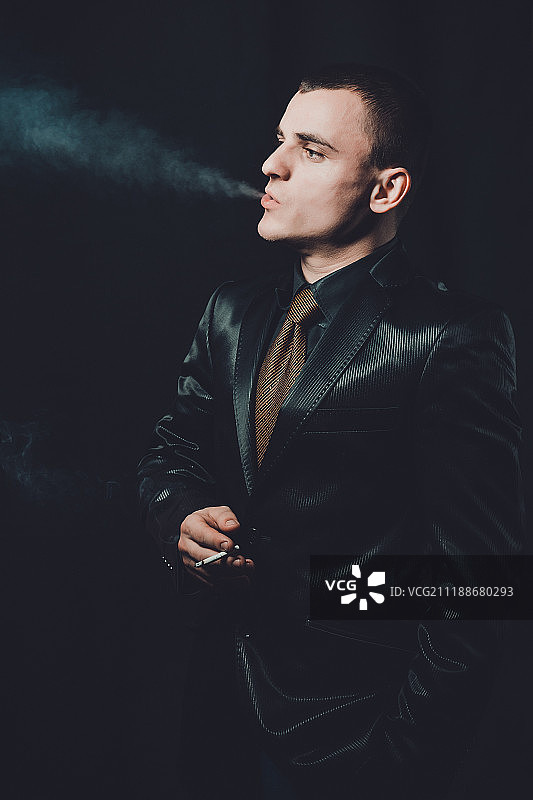 一个抽烟的年轻人，一个黑色的背景，一个经典的黑色西装图片素材