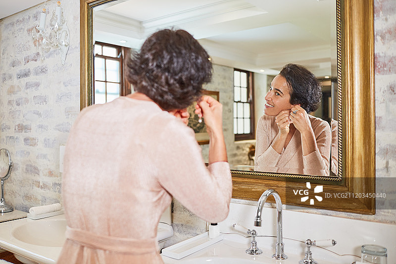 一个女人在酒店浴室的镜子前戴耳环图片素材