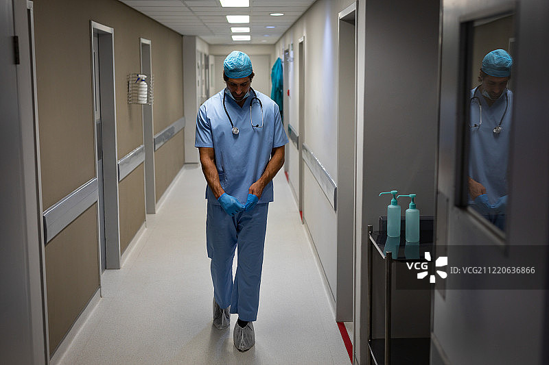 一个白人男性外科医生在穿过医院走廊时脱下他的橡胶手套图片素材