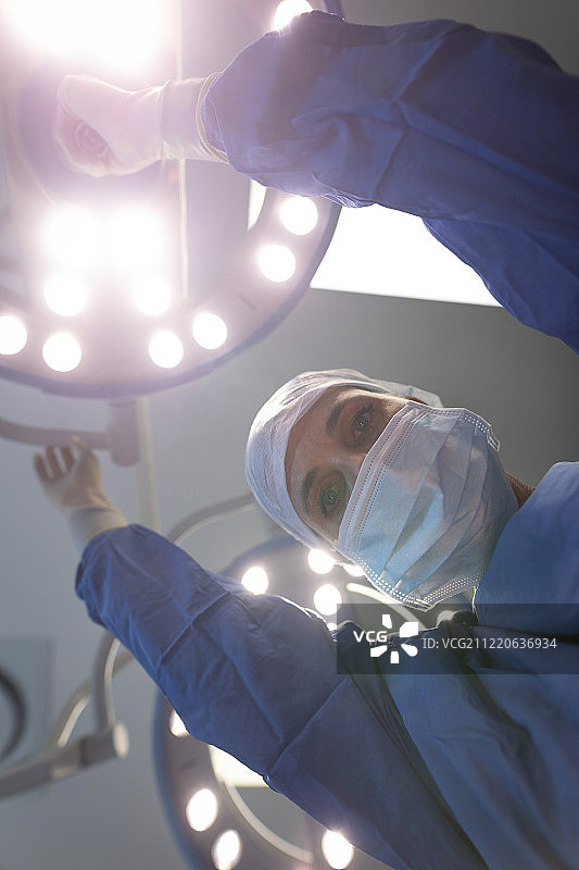 一名成熟的白种女外科医生在门诊移动手术灯时看着摄像机为手术做准备的低角度视图图片素材