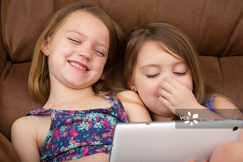 两个女孩一边看着平板电脑一边笑图片素材