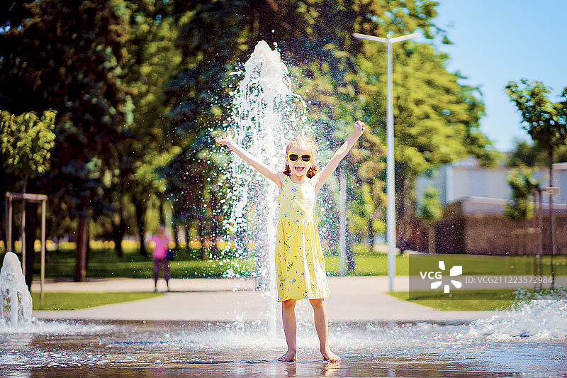 穿着黄色衣服的女孩在喷水池里玩得很开心图片素材