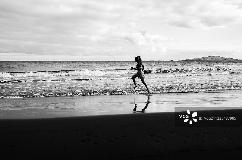沿着海岸跑的女人的侧视图图片素材