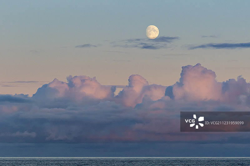 冰岛南部海岸日落时，一轮接近满月的月亮挂在粉红色的云上图片素材