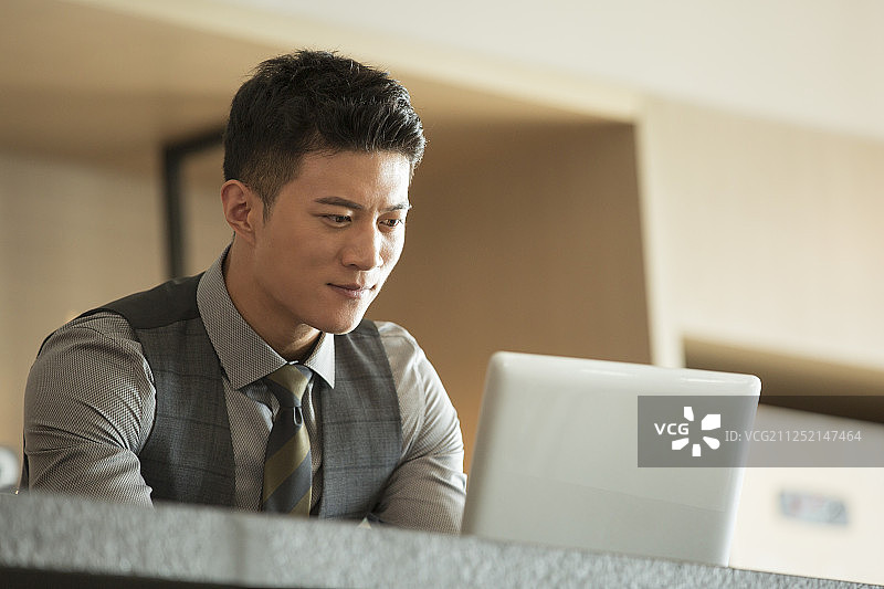一个青年商务男子使用笔记本电脑在酒店咖啡馆工作图片素材
