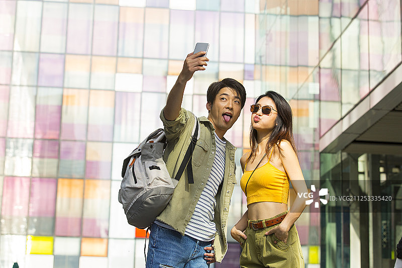 年轻情侣在户外商业街逛街旅游拿手机自拍图片素材
