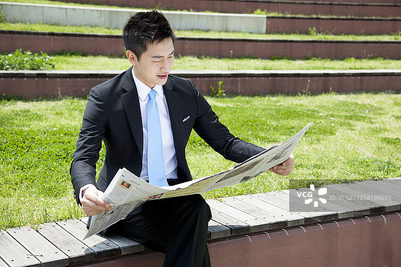 商人坐在长凳上看报纸的照片图片素材