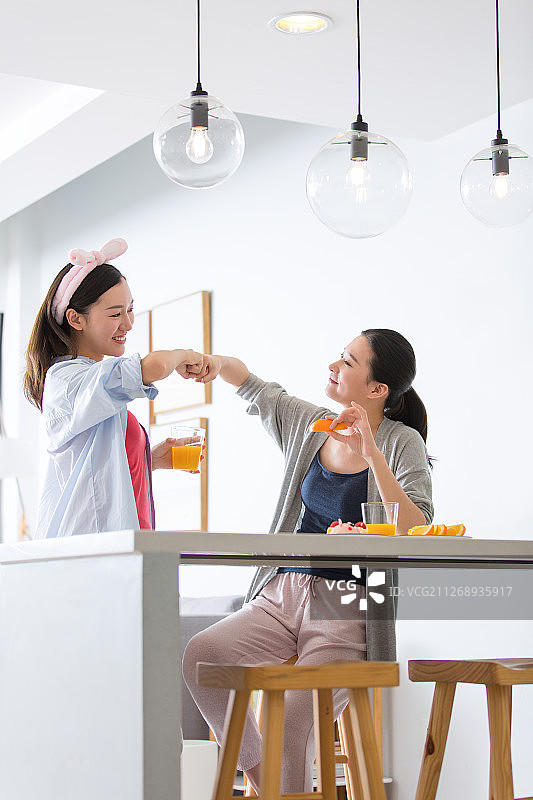 两个青年女子在起居室吧台吃橙子喝果汁顶拳聊天嬉戏图片素材