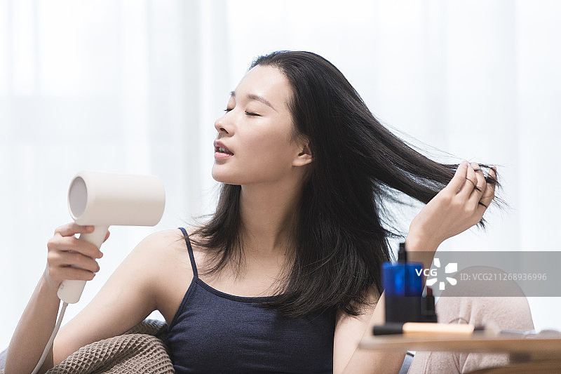 青年女子在客厅使用吹风机吹头发图片素材