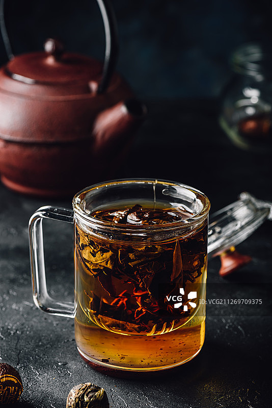 在玻璃杯中浸泡红茶，背景是茶壶图片素材