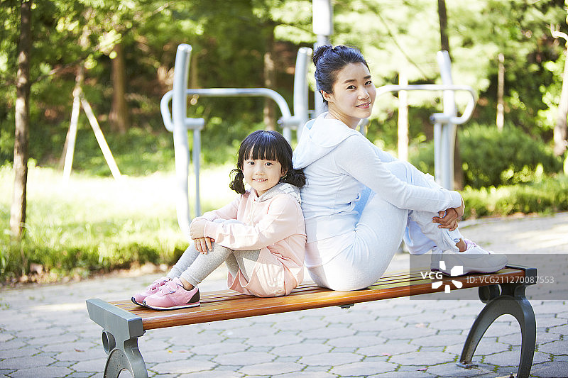 母亲和女儿背靠背坐在公园长椅上的照片图片素材