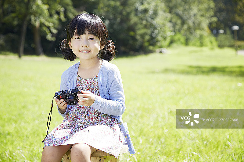 小女孩拿着相机在公园的草地上拍照图片素材