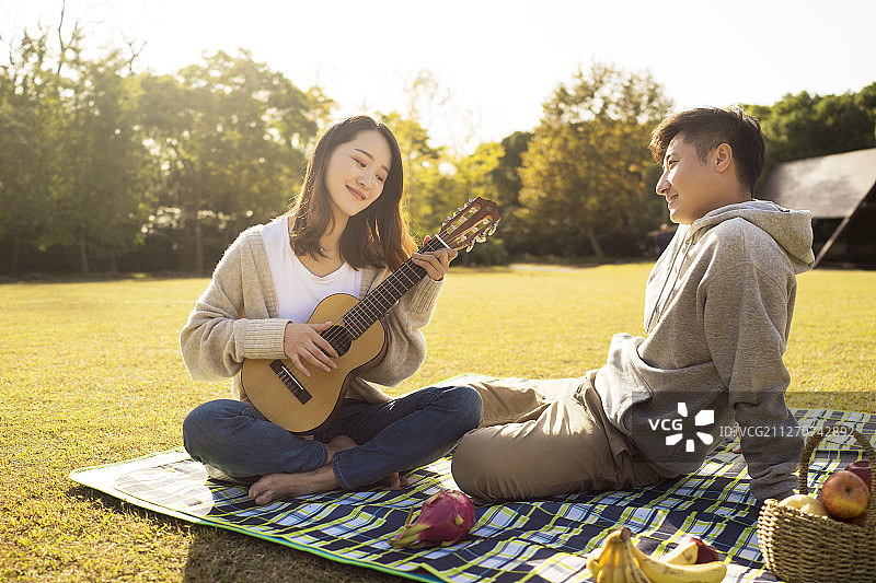 年轻情侣在草地上野餐演奏吉他图片素材