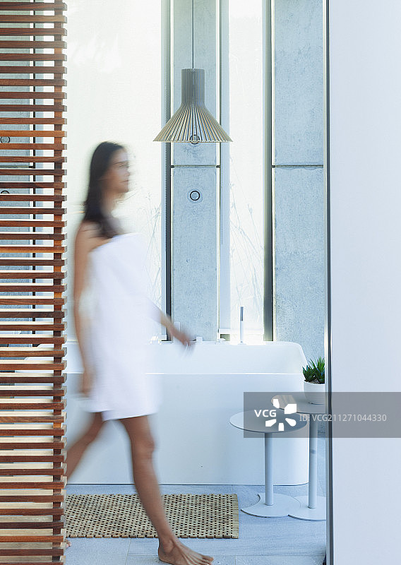 一个裹着毛巾的女人走在豪华现代的浴室里图片素材