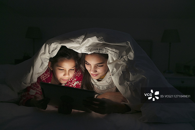 姐妹们在黑暗的卧室里，裹着毯子，在平板电脑上看电影图片素材