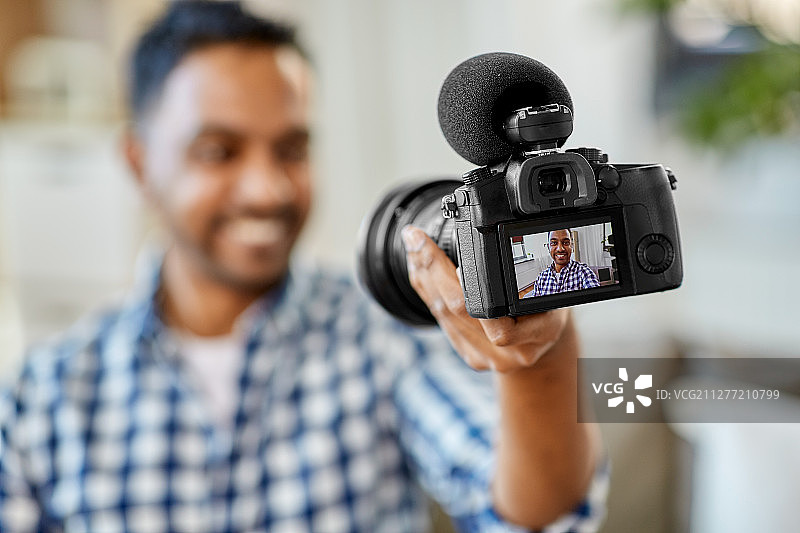 博客，视频博客和人们的概念-微笑的印度男性视频博客与相机视频博客在家里。男性视频博主用相机在家写博客图片素材