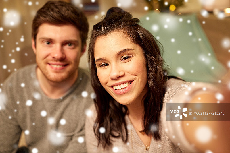 圣诞节和人们的概念-幸福的夫妇在家里自拍在雪。幸福的一对在家里自拍图片素材