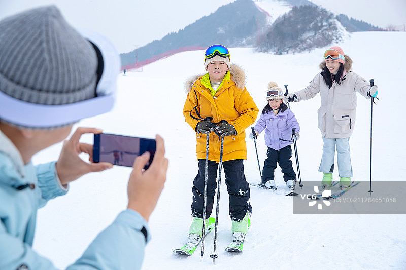 滑雪场上父亲用手机给孩子们和妻子拍照图片素材