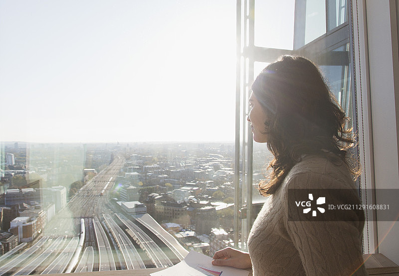 深思熟虑的女商人在阳光明媚的窗口俯瞰着城市图片素材