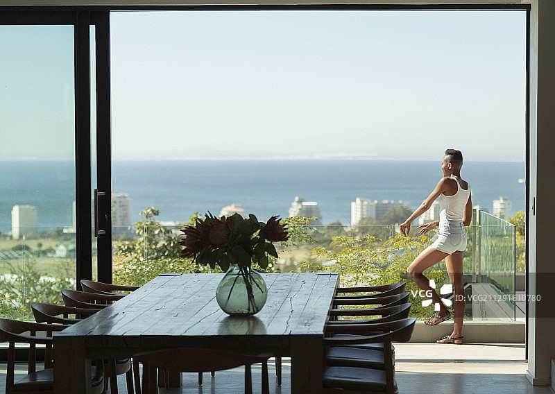年轻女子站在现代化的阳台上，可以看到阳光明媚的海景图片素材