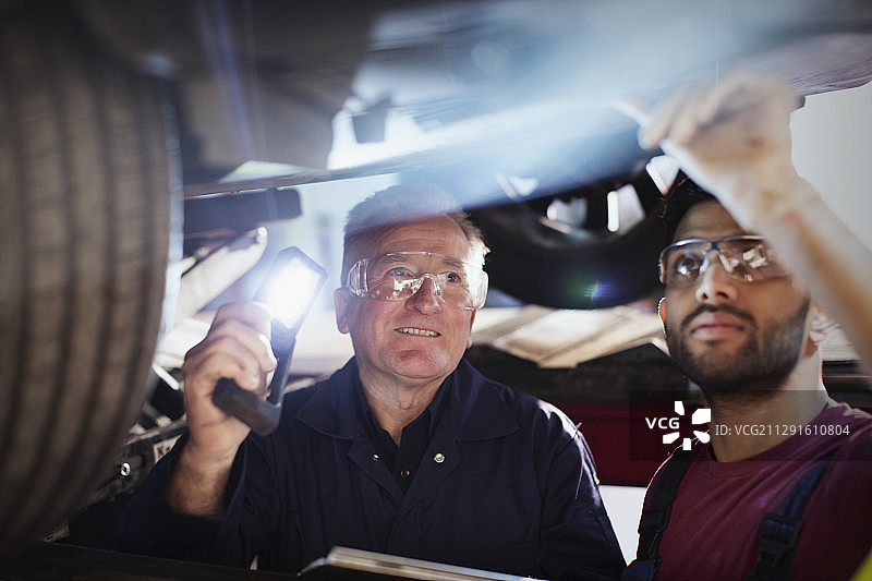 男机械师与手电筒在汽车修理厂下工作图片素材
